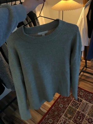 Grön/grå stickad tröja - En stilren grön-grå stickad tröja med rund halsringning och ribbade muddar. Tröjan har en rak passform och är perfekt för lager-på-lager. Materialet är mjukt och bekvämt.