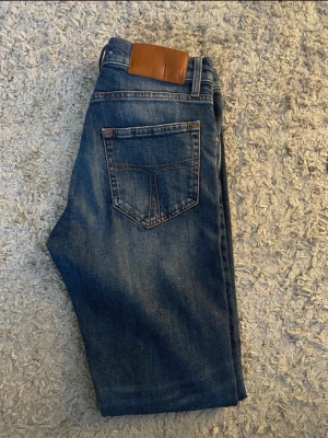 Selvedge jeans från Tiger of Sweden - Snygga blå jeans från tiger of Sweden med klassisk femficksdesign och bruna detaljer på bakfickan. Jeansen har en rak passform och är tillverkade i denim med en lätt tvättad look. Perfekta för en avslappnad stil. Nästan som nya! 