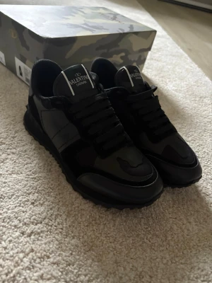 Svarta Valentino Garavani sneakers - Snygga svarta sneakers från Valentino Garavani med coola detaljer i läder och textil. Skorna har en chunky sula och klassisk låg profil med svarta skosnören och logga på plösen. Perfekta för dig som gillar exklusiv streetwear.