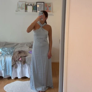 Ljusblå lång satinklänning - Säljer en elegant lång ljusblå satinklänning med halterneck! Passar perfekt till speciella tillfällen som gäst bröllopsklänning eller brudtärnaklänning! Helt oanvänd. 