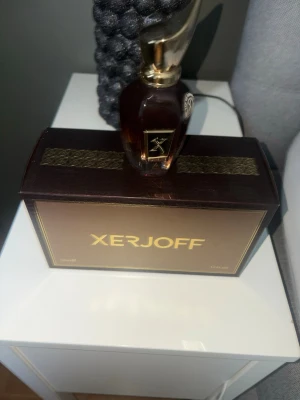 Xerjoff lyxig parfymflaska brun/guld - Exklusiv parfym från Xerjoff i en elegant mörkbrun glasflaska med gulddetaljer och unik, skulptural kork. Kommer i en lyxig ask med guldfärgad logga. Perfekt för dig som gillar exklusiva dofter och snygg design.