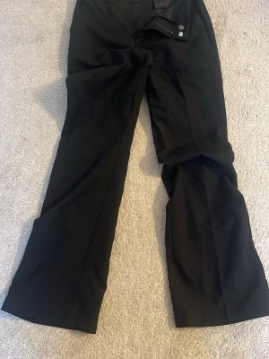 Svarta kostymbyxor från BikBok - Säljer ett par svarta kostymbyxor från BikBok i storlek 34. Byxorna har bootcut ben, diskret dragkedja och knapp framtill. Materialet är mjukt och har en lätt stretch för extra komfort. Perfekta för en clean och stilren look.