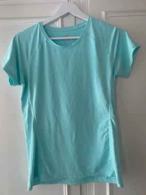 Träningströja (storlek 158/164) - En ljusblå t-shirt med rund hals och korta ärmar. Perfekt för träning eller aktiva dagar. Tillverkad i ett syntetmaterial som andas och ger en bekväm passform. I jättefint skick. 