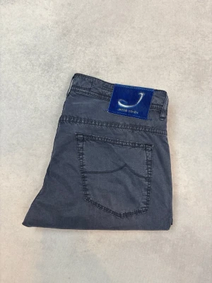 Mörkblå jeans från Jacob Cohen - Snygga mörkblå jeans från Jacob Cohen med raka ben och klassisk femficksmodell. Jeansen har en blå patch med logga bak i midjan och är tillverkade i ett mjukt bomullsmaterial. Perfekta för en avslappnad men stilren look.
