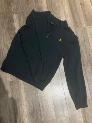 Mörkgrön halvzip från Lyle & Scott - Snygg mörkgrön tröja från Lyle & Scott med halvzip och gul logga på bröstet. Perfekt för en stilren och avslappnad look. Inga prisförslag är dumma!