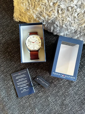 Tommy Hilfiger klocka - Säljer en stilren Tommy Hilfiger-klocka i mycket fint skick. Klockan är i princip som ny utan repor och har bara använts vid något enstaka tillfälle. Klassisk design med brun läderrem och ljus urtavla som passar både till vardag och mer uppklädda tillfällen. OBS behövs byta batteri på den resten är den i slipper ny skick😃