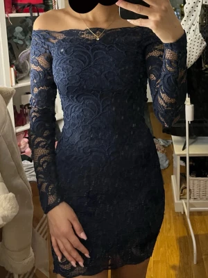 Marinblå klänning H&M - Säljer en marinblå kort klänning från H&M med offshoulder-design. Klänningen har långärmade spetsärmar och figurnära passform. Perfekt för dig som gillar eleganta detaljer och stilren look.