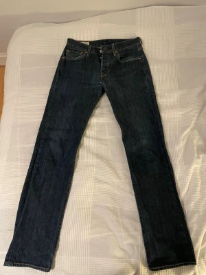 Mörkblå 501 jeans från Levi's - Säljer ett par klassiska mörkblå jeans från Levi's modell 501 med raka ben och femficksmodell. Jeansen har snygga kontrastsömmar och läderpatch bak i midjan. Perfekta till en avslappnad stil och passar till det mesta.