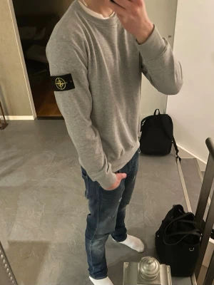 Grå tröja från Stone Island - Snygg grå Stone Island tröja i storlek M. Riktigt stilig och går att styla till nästan allt. Modellen på bilden är 180 cm 68kg. Priset är inte hugget i sten. Hör av er vid minsta lilla fundering!