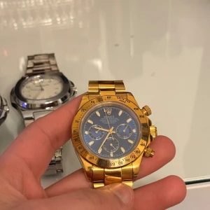 Herrklocka - Snygg herrklocka med kronograf och blå urtavla och guldfärgat armband och boett. Klockan har tre subdials, Perfekt för dig som gillar exklusiva accessoarer och vill sticka ut med en ikonisk design.