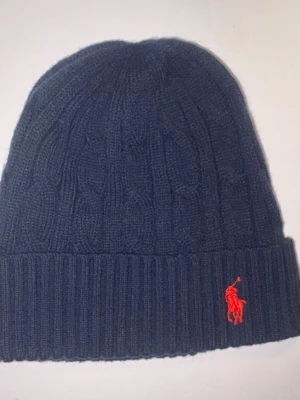 Mörkblå kabelstickad mössa Polo Ralph Lauren - Marinblå Polo Ralph Lauren mössa. Användt fåtal gånger och är som helt ny. Säljer pga inte jag använder den. Hör av vid frågor eller liknande!😁