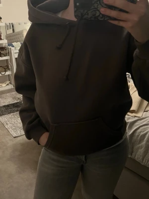 Mörkbrun hoodie med huva - Säljer en enkel och stilren mörkbrun hoodie med huva och dragsko. Hoodien har en stor magficka och ribbade muddar vid ärmslut och nederkant. Perfekt för dig som gillar en avslappnad och bekväm stil.