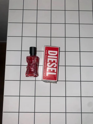 Diesel röd parfymflaska - Cool parfym från Diesel i en unik, röd glasflaska med svart kork. Flaskan har en modern och edgy design som sticker ut och kommer med originalförpackning i rött och vitt. Perfekt för dig som gillar statement-dofter och snygga detaljer på hyllan.