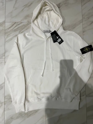 Stone island Hoddie - vit färg  - Helt ny stone island Hoddie i super fräsch och fin vit färg Inga fläckar eller liknande  Priset kan diskuteras 😊 Extra stone island badge följs med i köpet Längd på Hoddien: 65 cm Midjemått (armhåla till armhåla): 55 Ärmlängd: 63