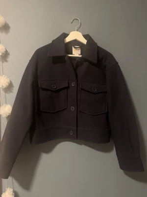 Mörkblå kort kappa från Gina tricot. - Snygg mörkblå kappa från Gina tricot med klassisk krage och stora bröstfickor med lock och knappar. Rak, något boxig passform och knäppning framtill. Perfekt lager på lager-plagg för kyligare dagar och nu för våren!💕💕