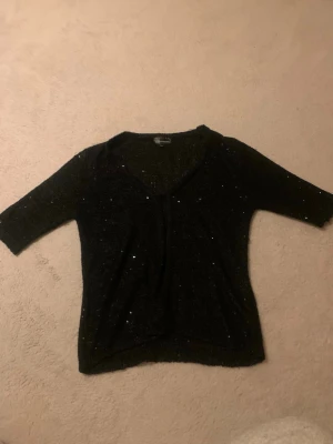 Svart glittrig stickad kofta KappAhl - Snygg svart stickad tröja från KappAhl med glittriga inslag. Tröjan har trekvartsärmar och en djupare v-ringning. Perfekt för dig som vill ha något enkelt men ändå lite extra. Mjuk och stretchig kvalitet.