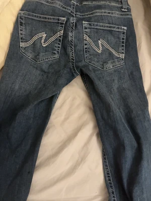 Blå jeans med broderade bakfickor - Ett par klassiska blå jeans med raka ben och snygga broderade detaljer på bakfickorna i vitt. Jeansen har normal midja och är tillverkade i slitstark denim. Perfekta för dig som gillar en enkel men ändå unik look.