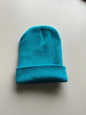 Turkos ribbstickad mössa - Snygg turkos mössa i ribbstickad modell med uppvikt kant. Perfekt för att hålla värmen och ge en poppig färg till din outfit. Enkel och stilren design utan synligt märke, passar till de flesta stilar.