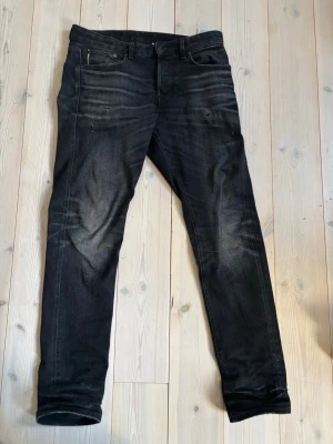 Svarta Jack and Jones jeans i premium salvadge  - Säljer ett par svarta slim fit jeans med snygga slitningar och tvättade detaljer. Klassisk femficksmodell ned knapp i midjan. Jeansen har en modern passform och är perfekta för en trendig vardagslook.