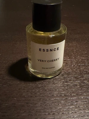 ESSNCE Very Cherry Eau de Parfum - ESSNCE Very Cherry Eau de Parfum i en stilren, rund glasflaska med svart lock. Parfymen har en ljusgul vätska och etiketten är enkel med svart text. Doften har tydliga körsbärstoner och passar dig som gillar fruktiga parfymer.