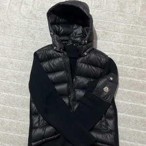 Moncler cardigan/dunväst - Snygg svart dunväst från Moncler med huva och stickade sidor. Storleken är M men funkar även för S. jag är 173cm 75kg och den sitter perfekt på mig. Priset är inte hugget i sten!!!