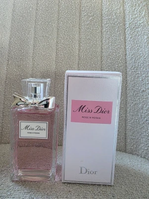 Miss Dior Rose N'Roses parfym - Miss Dior Rose N'Roses från Dior är en elegant parfym i en rektangulär glasflaska med ljusrosa doftvätska. Flaskan har en silverfärgad rosett vid halsen och kommer med en vit och rosa kartong. Perfekt för dig som älskar fräscha och blommiga dofter.