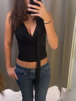 Svart croppad halterneck topp - Snygg svart croppad halterneck topp med djup v-ringning och knytband i nacken. Toppen har en tight passform och är perfekt för att skapa en trendig look. Passar till både jeans och kjol.