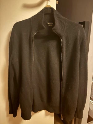 Massimo Dutti Kashmir blandning - Stilren svart ziptröja från Massimo Dutti med hög ribbad krage och långa ärmar. Tröjan är tillverkad i mjukt material och har en rak passform med dragkedja framtill. Perfekt för lager på lager och enkel att matcha.