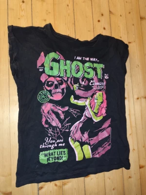 Svart t-shirt bandtröja Ghost - Cool svart band t-shirt med färgstarkt tryck av texten 'Ghost' och en tecknad serieinspirerad design i grönt, rosa och vitt. T-shirten har korta ärmar och en avslappnad passform. Perfekt för dig som gillar unika och grafiska motiv.