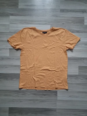 Orange basic t-shirt i bomull - En enkel och stilren orange t-shirt från H&M. T-shirten har rund halsringning och korta ärmar, tillverkad i mjuk bomull för en skön känsla. Perfekt att matcha med jeans eller shorts för en avslappnad look.