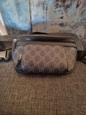 Gucci GG Supreme shoppingväska grå - Snygg shoppingväska från Gucci i mörkgrått GG Supreme-mönster. Väskan har justerbar axelrem, två dragkedjefack och detaljer i svart läder. Perfekt för dig som vill ha en stilren och lyxig accessoar med ikoniskt mönster. Alldrig använd