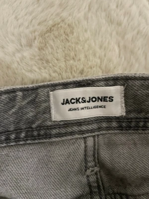 Grå jeans från Jack & Jones - Snygga grå jeans från Jack & Jones med klassisk femficksmodell. Jeansen har en tvättad look och är tillverkade i bomullsmix för skön passform. Perfekta för dig som vill ha en stilren och avslappnad vibe.
