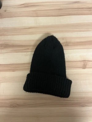 Svart ribbstickad mössa - En klassisk svart ribbstickad mössa med uppvikt kant. Mössan har en enkel och stilren design som passar till det mesta. Perfekt för kalla dagar och enkel att matcha med olika outfits.