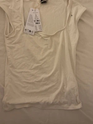 Vit ärmlös linnetopp Gina Tricot - Säljer en enkel och stilren vit linnetopp från Gina Tricot. Toppen är ärmlös med rund halsringning och tillverkad i mjukt material som känns skönt mot huden. Perfekt att matcha med jeans eller kjol för en clean look.