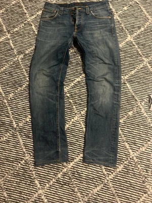 Blå raka jeans med slitningar - Säljer ett par blå jeans med raka ben och snygga slitningar. Jeansen har klassisk femficksmodell, orangea sömmar och normal midja. Perfekta för en avslappnad och trendig look.