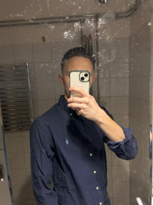 Mörkblå skjorta från Ralph Lauren - Snygg mörkblå skjorta från Ralph Lauren med klassisk passform och knappar framtill. Skjortan har lång ärm och den ikoniska loggan broderad på bröstet. Perfekt för en stilren look. Villig att gå ner lite i pris för snabb affär!