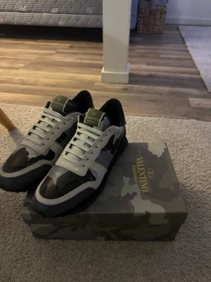 Valentino Garavani camo sneakers - Snygga sneakers från Valentino Garavani med svart, grått och vitt camomönster. Skorna har vita snören, svart sula och detaljer i mocka och läder. Klassisk låg modell med logga på plösen och cool design som sticker ut.