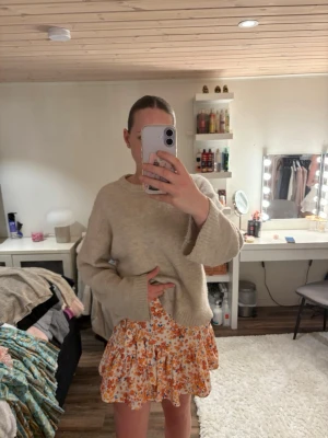 Blommig volangkjol i orange och vitt - Superfin kort kjol med blommigt mönster i orange, vitt och blått. Kjolen har volangdetaljer och resår i midjan för en bekväm passform. Perfekt för vår och sommar, lätt och luftig i materialet.