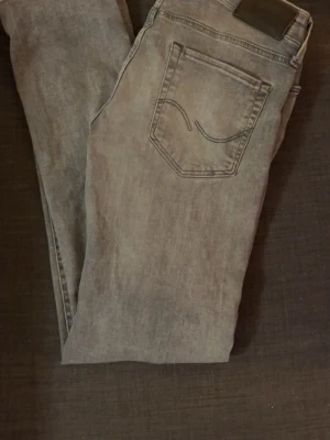 Ljusgrå raka jeans med bakfickor - Säljer ett par ljusgrå jeans med raka ben och klassiska bakfickor med snygga sömmar. Jeansen har en diskret tvättad look och är tillverkade i bomull. Perfekta för en avslappnad och trendig stil.