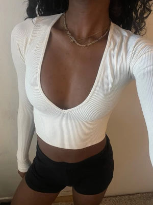 Vit ribbad croppad långärmad topp - Säljer en vit croppad topp med djup v-ringning och långa ärmar. Toppen är ribbad och har en tight passform som framhäver figuren. Perfekt för dig som gillar trendiga och stilrena plagg.