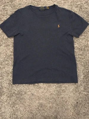 Mörkblå t-shirt från Polo Ralph Lauren - Snygg mörkblå t-shirt från Polo Ralph Lauren med klassisk rund halsringning och den ikoniska broderade loggan i gult på bröstet. Tillverkad i mjuk bomull för en bekväm känsla och enkel passform. Perfekt basplagg till garderoben.