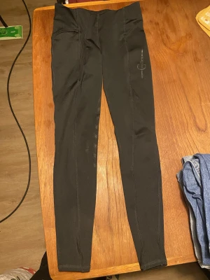 Svarta ridtights från covalliero - Säljer ett par svarta ridtights från Covalliero med silikonprint på insidan av benen för extra grepp. Tightsen har en liten ficka med dragkedja och diskret logga på låret. Perfekta för ridning och träning.