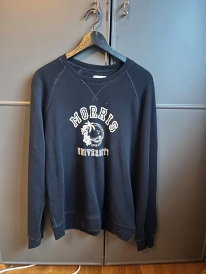 Mörkblå sweatshirt Morris  - Cool svart sweatshirt från Morris med trycket 'Morris University' och palmtryck framtill. Tröjan har rund halsringning, långa ärmar och ribbade muddar vid ärmslut och nederkant. Perfekt för en avslappnad och trendig look.