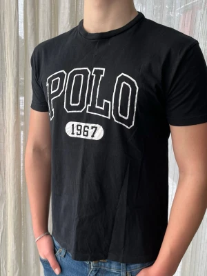 Svart Ralph Lauren T-shirt, storlek s - Svart Ralph Lauren T-shirt med vitt tryck i 100% bomull  Mycket bra skick, inga defekter förutom att trycket spruckit lite (syns på bild)                               Storlek S                                                                  Axelbredd: 48 cm Längd: 66 cm