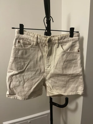 Vit högmidjade jeansshorts - Snygga vita jeansshorts med hög midja och klassisk femficksdesign. Gjorda i ett stadigt bomullstyg, perfekta för varma dagar. Stängs med knapp och dragkedja framtill. Enkla att matcha med allt i garderoben.