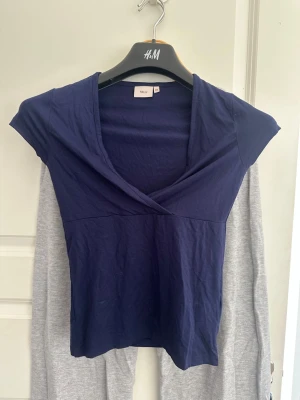 Mörkblå omlottopp från Nelly - Mörkblå omlottopp från Nelly med v-ringning och korta ärmar. Topp i mjuk bomull med figurnära passform, perfekt till jeans eller kjol. Enkel och stilren design som passar till många olika looks.