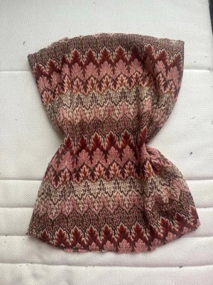Vinröd mönstrad tubtopp - Tubtopp med detaljerat mönster i vinrött, rosa, beige och brunt. Ärmlös och figurnära modell som ger en unik retrovibe till din outfit. Den är handsyd och det finns bild på sömmen. Den är lite fransig men det syns inte när den sitter på.