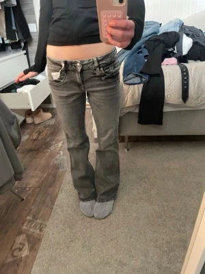 Grå bootcut jeans med låg midja - Säljer ett par grå bootcut jeans med slitna detaljer och låg midja. Jeansen har klassiska fem fickor och silverfärgad knapp. Perfekta för en avslappnad och trendig look.