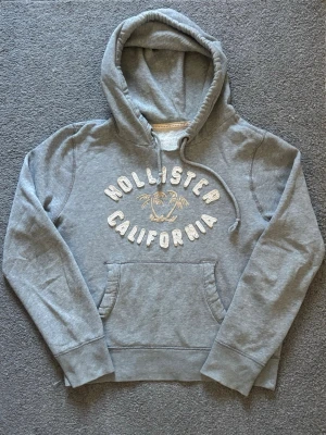 Vintage Hollister Hoodie - Sällynt och Vintage Hollister Hoodie! | Palmträd i mitten av textryck centrerat på hoodien🌴| Mycket bra skick förutom en fläck på högra ärmen, syne ej mkt alls, se sista bild | Storlek S | Perfekt till hösten | Längd ≈60 cm, Bredd 53cm | Modell 175cm, 68kg Priset ej hugget i sten!