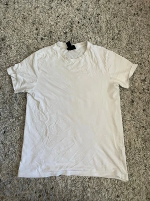 Vit basic t-shirt från H&M - En klassisk vit t-shirt från H&M i regular fit. Tillverkad i mjuk bomull med rund halsringning och korta ärmar. Perfekt att matcha med jeans eller shorts för en enkel och clean look.